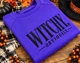 Close-up of Witchy Obviously black embroidered lettering on a purple Gildan Halloween sweatshirt, showing the stitched design.